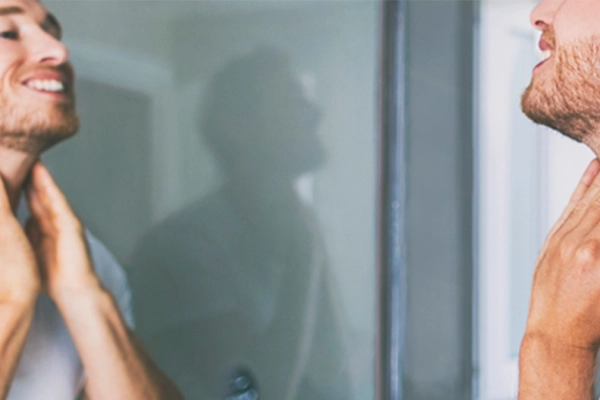 Junger Mann begutachtet vor dem Spiegel sein Gesicht